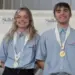 Christiansen and Often Take Gold - Carroll News | Carroll Publications | Carroll County, MD Two smiling SkillsUSA competitors wearing blue shirts with gold medals on stage beside a first-place sign.