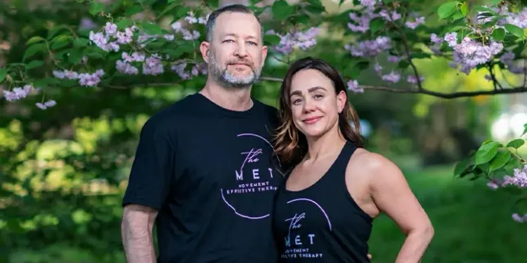 MET_FeaturedImage - Carroll News | Carroll Publications | Carroll County, MD Two adults in black The MET shirts posing outdoors under flowering pink blossoms, smiling at the camera.