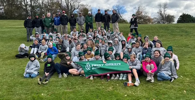first-green-golf-image - Carroll News | Carroll Publications | Carroll County, MD Large group of students and instructors posing on a grassy hill, holding a green First Green banner.