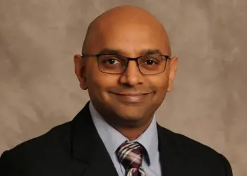 Professional head-and-shoulders portrait of a smiling man wearing glasses, a suit, and striped tie.