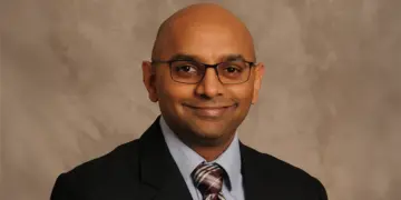 Professional head-and-shoulders portrait of a smiling man wearing glasses, a suit, and striped tie.