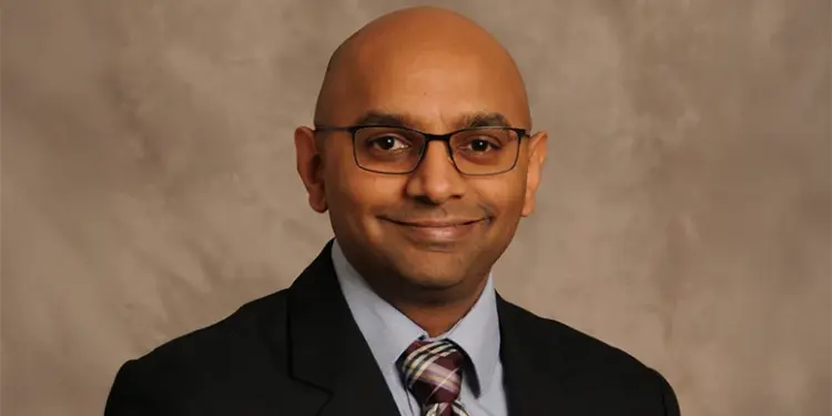 Professional head-and-shoulders portrait of a smiling man wearing glasses, a suit, and striped tie.