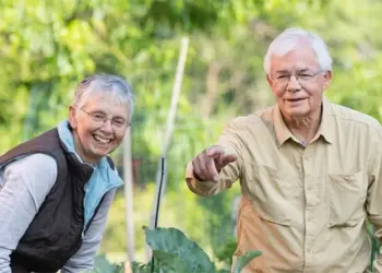 Two smiling seniors gardening together in a lush outdoor yard.
