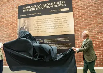 Two people unveil a plaque for the McDaniel College Kahler Nursing Education Center against a brick wall outside a hospital setting.