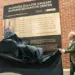 Two people unveil a plaque for the McDaniel College Kahler Nursing Education Center against a brick wall outside a hospital setting.