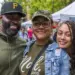 Jerome-Heidi-Whiting-Aniyah-Clark - Carroll News | Carroll Publications | Carroll County, MD Three smiling friends posing at an outdoor market with tents in the background, wearing casual outfits and caps.