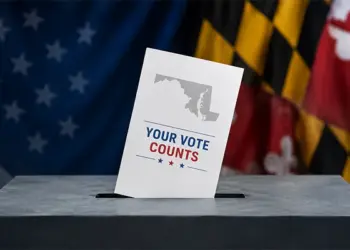 Ballot being dropped into a ballot box with a 'Your Vote Counts' card, patriotic flags in the background.