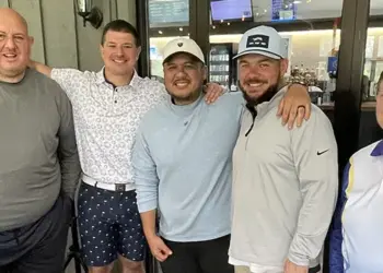Five adults posing with arms around each other in a cafe, smiling at the camera.