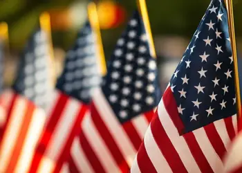 Rows of American flags on flagpoles, close-up foreground flag with others blurred in the background at a patriotic display