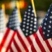 Rows of American flags on flagpoles, close-up foreground flag with others blurred in the background at a patriotic display