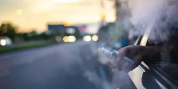 Person vaping from a car window at sunset, with vapor plume filling the air outside the vehicle.