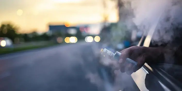 Person vaping from a car window at sunset, with vapor plume filling the air outside the vehicle.
