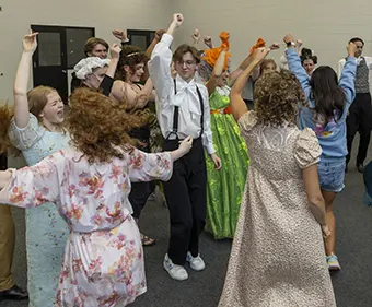 BTS Warmup_image - Carroll News | Carroll Publications | Carroll County, MD Group of people dancing together in a room, wearing party outfits and costumes, arms raised in the air.