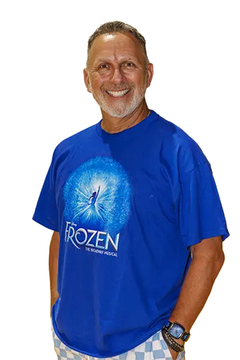 Homero Bayarena_headshot - Carroll News | Carroll Publications | Carroll County, MD Smiling man with gray beard wearing a blue Frozen-themed t-shirt, standing with his hands by his sides. **(informative)**
