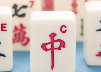 Close-up of white Mahjong tiles, with the red '中' tile centered and other tiles showing Chinese characters in the background.