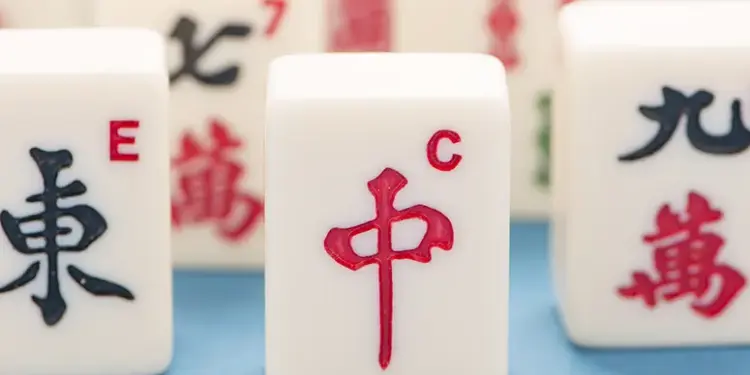 Close-up of white Mahjong tiles, with the red '中' tile centered and other tiles showing Chinese characters in the background.