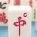 Close-up of white Mahjong tiles, with the red '中' tile centered and other tiles showing Chinese characters in the background.