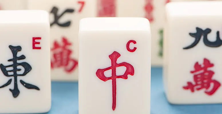 Close-up of white Mahjong tiles, with the red '中' tile centered and other tiles showing Chinese characters in the background.