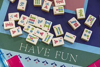Pile of white domino-like tiles with colorful symbols scattered on a teal game surface that reads'HAVE FUN'.