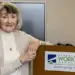 Smiling older woman stands at a podium with a Carroll County Workforce Development sign in a conference room.