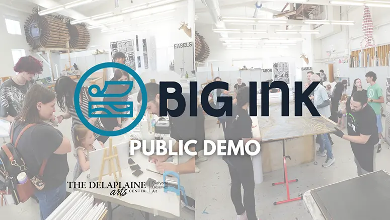 Busy art studio during a Big Ink public demo; people watch and work on printmaking projects, with a Delaplaine Arts Center banner visible.