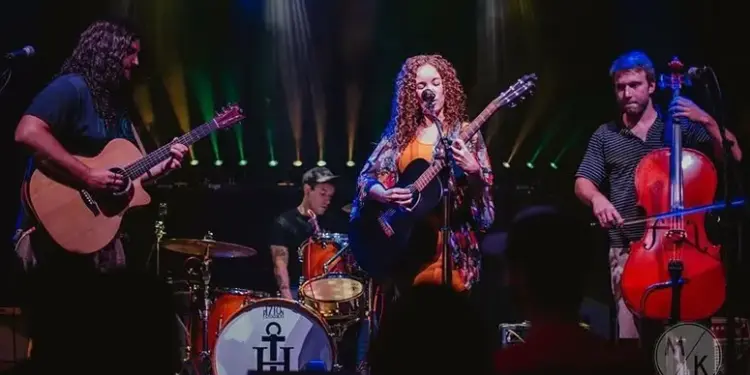Ebb & Nova - Carroll News | Carroll Publications | Carroll County, MD Live band on stage: a female guitarist/vocalist center stage with two guitarists and a cellist, drummer in back, colorful stage lights behind them