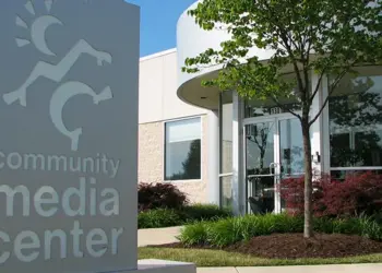 Front view of a community media center with a tall sign reading 'community media center' and a landscaped entrance with glass doors and trees.