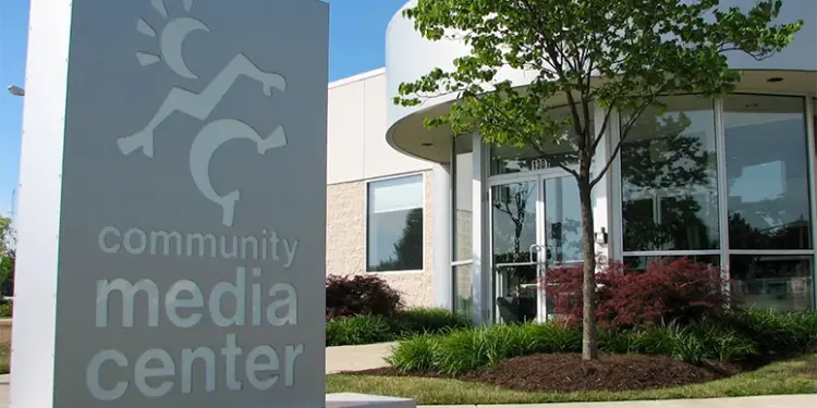 Front view of a community media center with a tall sign reading 'community media center' and a landscaped entrance with glass doors and trees.