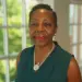 Sandra-ThomasLalmansingh - Carroll News | Carroll Publications | Carroll County, MD Portrait of a smiling woman wearing a teal sleeveless top and pearl necklace, indoors by a window.