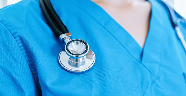 Stethoscope resting on blue medical scrubs, ready for exam.