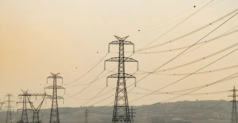 Series of tall metal transmission towers carrying high-voltage lines across a hazy sunset landscape.###