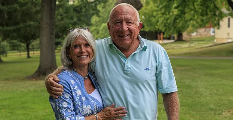 Older couple smiling and embracing in a sunny grassy park.
