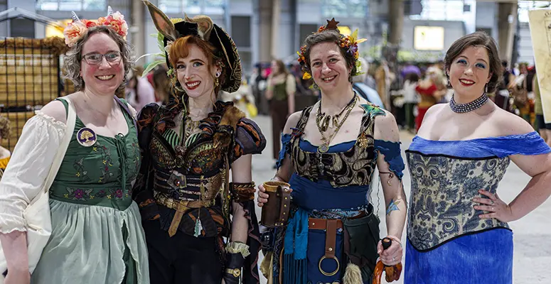 Four women in colorful renaissance costumes pose together at an indoor festival.