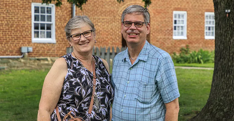 Smiling older couple standing on a lawn in front of a brick building on a sunny day
