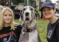Girl in a Metallica shirt poses with a large Great Dane and a smiling woman at an outdoor festival in a park.