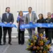 Group of ten adults in business attire participate in a ribbon-cutting ceremony for Carroll Community College, with a blue ribbon and a colorful flower arrangement at the front.