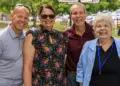 Four adults smiling and posing outdoors at a park event, standing side by side (two men on sides, two women in the middle).