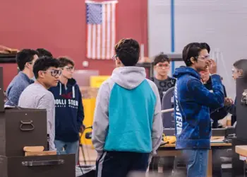 ccps-career-tech-image - Carroll News | Carroll Publications | Carroll County, MD Group of students in a machine shop standing around workbenches and equipment, discussing a project, with an American flag in the background.