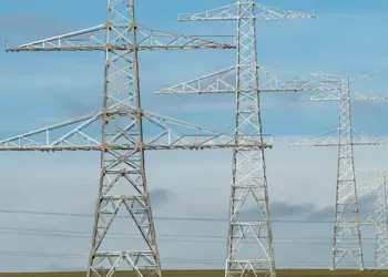 Metal lattice transmission towers carrying high‑voltage lines across a flat field under a blue sky.