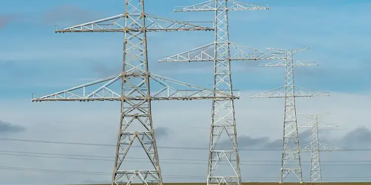 Metal lattice transmission towers carrying high‑voltage lines across a flat field under a blue sky.