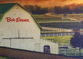 White barn with a green roof labeled 'Bob Evans' in a fenced rural farm landscape.