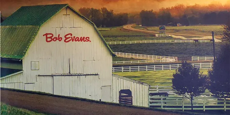 White barn with a green roof labeled 'Bob Evans' in a fenced rural farm landscape.