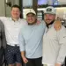 Five adults posing with arms around each other in a cafe, smiling at the camera.