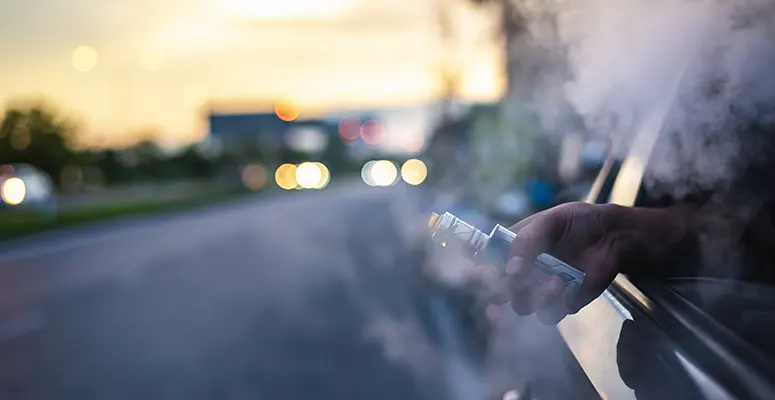 Person vaping from a car window at sunset, with vapor plume filling the air outside the vehicle.